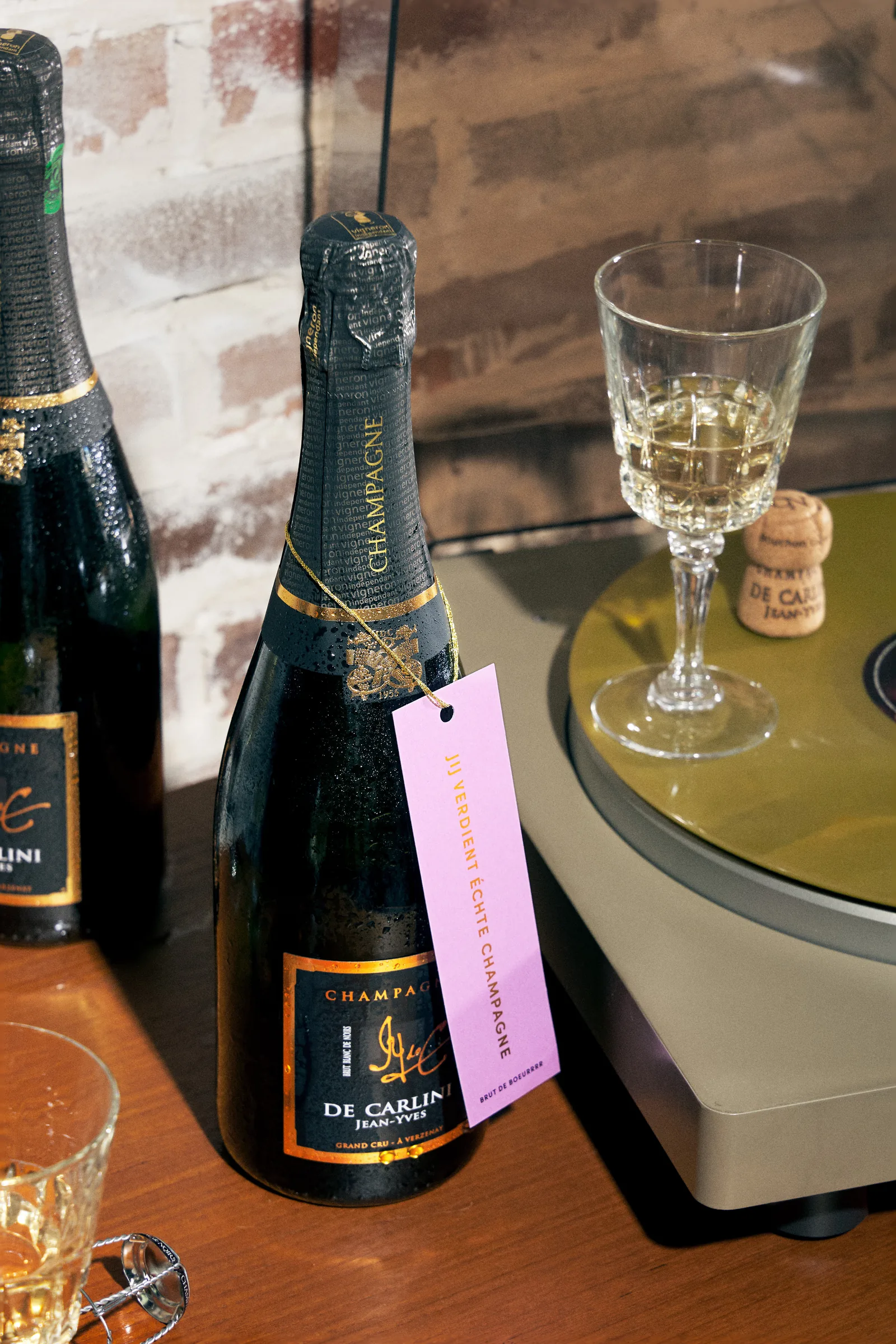 Fles champagne met roze halslabel naast een glas champagne en een platenspeler